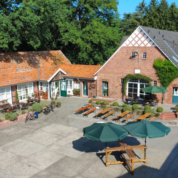 Luftaufnahme eines gemütlichen Hofcafés mit Außenterrasse, rustikalen Backsteingebäuden und Sitzplätzen im Grünen.